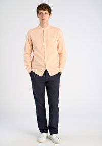  Licht perzikkleurig overhemd met knopen, voorzien van een enkele borstzak, gecombineerd met donkerblauwe chino's en witte sneakers. Strak ontwerp met lange mouwen.