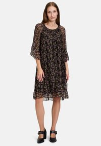 Mustat kukkakuosiset mekko, jossa on läpikuultavat hihat, ristimäinen kaula-aukko ja röyhelöinen helma. Mekossa on hienovarainen kuvio pienistä värikkäistä kukista.