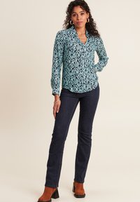 Langarm, knoopshirt in teal met een zwart abstract patroon, gecombineerd met donkere jeans en bruine hoge laarzen. Glad stofgevoel.