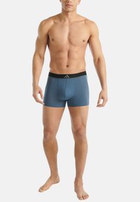 Herrarnas blå boxertrosor i mjukt tyg, med ett svart elastiskt midjeband med grå detaljer och en åtsittande design.