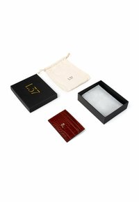 Porta carte in pelle rossa con motivo coccodrillo testurizzato, logo dorato, accompagnato da una scatola nera e una custodia con cordoncino color crema.