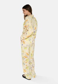 Combinaison florale jaune avec des accents orange et violet, présentant un design avec col, une taille élastique et des poches latérales. Texture douce.