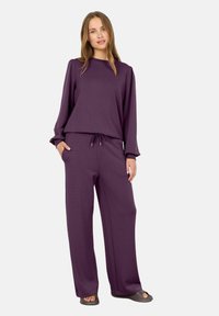 Conjunto de salón púrpura que incluye una parte superior de manga larga con cuello redondo y pantalones de corte relajado con cinturilla ajustable mediante cordón. Tejido texturizado.