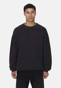 Maglione a coste grigio scuro con scollo rotondo, spalle scese e maniche lunghe, abbinato a pantaloni neri.