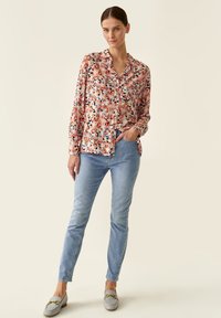 Blomstret langærmet skjorte i pink, blå og sort på en lys baggrund, parret med lyseblå jeans og grå loafers med gyldent hardware.