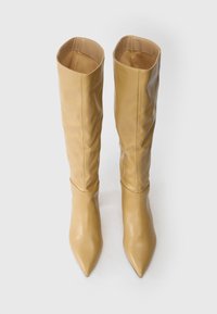 Ζευγάρι ψηλών, μπεζ δερμάτινων μπότες με μυτερούς αντίχειρες, που στέκονται όρθιες σε λευκό φόντο.