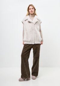 Gilet in pelliccia sintetica grigia chiara con colletto alto e zip frontale, abbinato a pantaloni larghi a stampa leopardata marrone e scarpe platform grigie spesse.