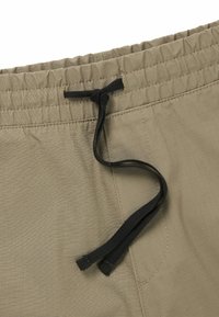 Pantaloni corti beige con vita elastica, dotati di un laccio nero e un sottile motivo testurizzato. Include dettagli cuciti.