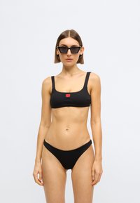 Haut de bikini noir côtelé avec larges bretelles et petit logo ; bas de bikini taille basse assorti. Les deux pièces sont en tissu texturé.