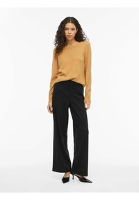 Pruun, pika varrukaga kootud sviiter laeva kaelusega, millele on kombineeritud mustad kõrge vöökohaga laiad püksid ja terava ninaga mustad kõrged kontsad.