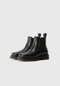 Black leather Chelsea boots feature elastic side panels, rounded toes, and pull tabs. The sole has a textured grip for traction.