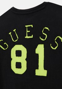 T-shirt in cotone nero con ricamo verde neon che riporta la scritta "GUESS" e il numero "81". Design a girocollo con una finitura testurizzata.