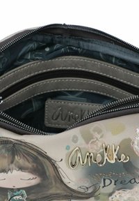 Borsa beige con un'esterno testurizzato che presenta un personaggio illustrato. L'interno ha una fodera blu scuro e diversi scomparti con zip.