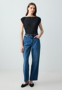 Top plissettato nero con scollatura ampia, abbinato a jeans blu a gamba dritta. Presenta una cintura nera e ballerine nere. Design minimalista, texture lisce.