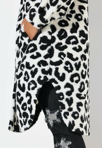 Uldent hvid og sort leopardmønstret frakke med sideslidser, der har lommer og en afslappet pasform, parret med slidte sorte jeans.