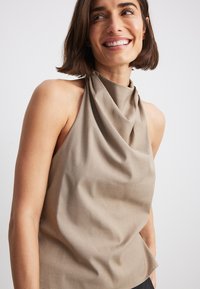 Beige halterneck-top med draperad halsringning, tillverkad av slät tyg. Har en avslappnad passform och minimalisk design.