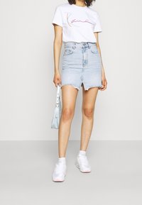 Jasnoniebieska spódnica dżinsowa z postrzępionym dołem i szczeliną z przodu, zestawiona z białą koszulką z wielobarwnymi liniami. Białe sneakersy i jasnoniebieska torebka.