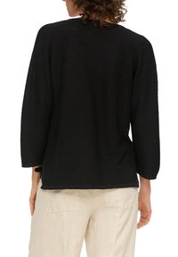 Schwarzer Pullover mit einem strukturierten Strickmuster, langen Ärmeln, einem runden Halsausschnitt und einer lässigen Passform, kombiniert mit hellen Hosen.