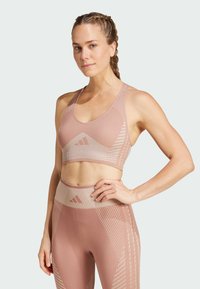 Sostén deportivo de color rosa claro con un patrón geométrico y textura acanalada. Combina con leggings de cintura alta que presentan elementos de diseño similares.
