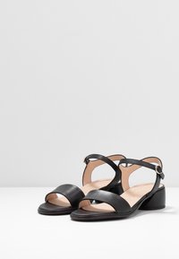 Mustat nahkaiset sandaalit, joissa on kaksi leveää hihnaa edessä, nilkkahihna soljella ja matala lohkoheel. Suora pinta ja neutraali sisävuori.