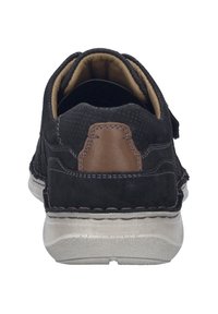 Schwarzer Wildlederschuh mit braunem Lederakzent an der Ferse, runde Form, gepolsterter Innenraum und strukturierte Sohle. Stichdetails entlang der Kanten.