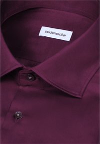 Col de chemise violet foncé et boutons supérieurs visibles avec une étiquette blanche à l'intérieur affichant le nom de la marque seidensticker.