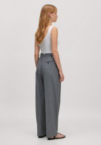 Graue weit geschnittene Hose aus strukturiertem Stoff, hohe Taille und zwei Gesäßtaschen, kombiniert mit einem weißen Tanktop und schwarzen Sandalen.
