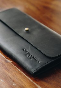 Black leather wallet with a flap closure, featuring a button clasp and embossed "HOLZRICHTER BERLIN." Smooth texture, minimalistic design.