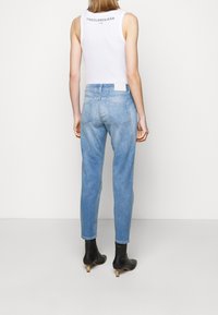 Jeans de color azul claro con un ajuste slim, cintura media y diseño de cinco bolsillos. La parte trasera presenta una etiqueta de cuero blanca y detalles de costura simples.