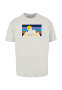 Lys grå t-shirt med et grafisk design i blå, orange og gul, der viser en sol og bjerge, samt teksten "JUST RHYSE" i fed gul.
