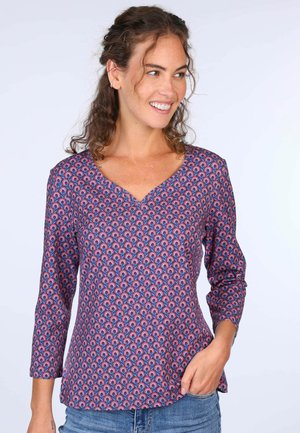 Lila gemusterte Bluse mit V-Ausschnitt und Dreiviertelärmeln. Das Design weist ein sich wiederholendes Muster in roten und blauen Tönen auf. Glatte Stofftextur.