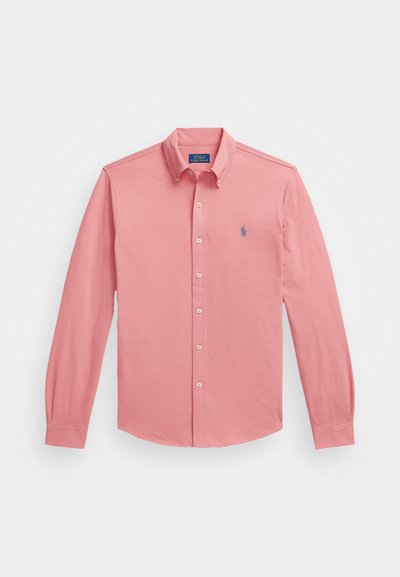 Svetloružová, dlhá košeľa s gombíkmi vyrobená z bavlny s špicatým golierom, obsahujúca malé modré logo na ľavej hrudi.