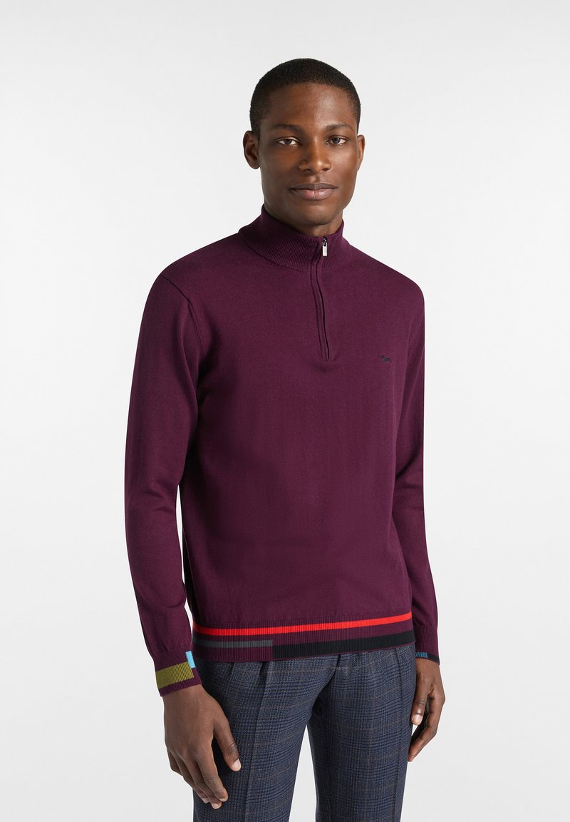 Lila, langärmliger Reißverschluss-Pullover mit geripptem Kragen und farbigen Streifenakzenten in Rot, Grün und Blau am Saum und an den Bündchen.
