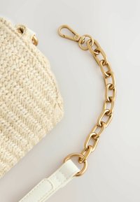 Fonott bézs szalmakézitáska sima fehér bőrpánttal és aranyszínű láncszemes díszítéssel, kapoccsal ellátva.
