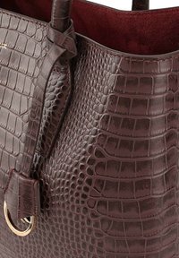 Donker bordeaux lederen tote bag met een krokodillenstructuur, met een geknoopte strap en een metalen ringaccent. Glad interieur.