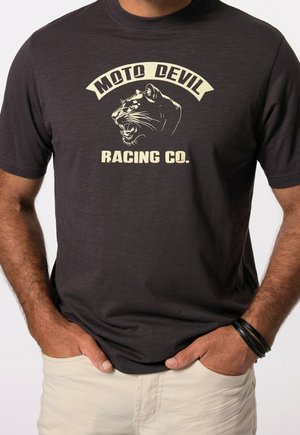 Mand iført en mørk t-shirt med et brølende panterhoved og teksten "Moto Devil Racing Co." i lys farve på brystet.