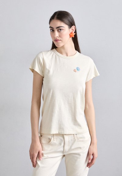 T-shirt en coton crème à manches courtes, avec un petit motif de coquillage bleu et corail sur la poitrine. Texture lisse et coupe décontractée.