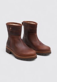 Botas de cuero marrón hasta el tobillo con puntera redondeada, forro interior suave y suela de goma texturizada. Presentan un logotipo en el lateral.