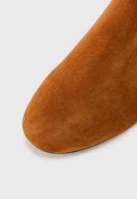 Bruine nubuck enkelboot met een gladde textuur, spitse neus en naadloos ontwerp. De zool is zwart en plat.