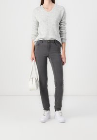 Vaqueros ajustados grises, suéter de punto gris claro con cuello en V, bolso blanco y zapatillas blancas. Textura suave, diseño ceñido.