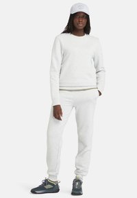 Sweat-shirt gris clair et joggings assortis en tissu doux. Assortis avec une casquette gris clair. Les chaussures présentent des tons foncés avec des accents verts.