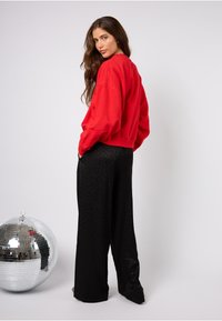 Červená volná mikina s nízkými rameny spojená s černými širokými kalhotami s jemným leopardím vzorem. Vedle stříbrný disco míč.