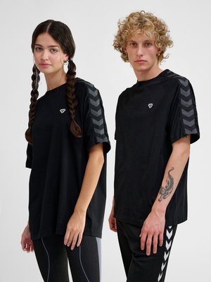 Ung kvinde med fletninger og ung mand med krøllet hår bærer matchende sorte t-shirts med v-mønster på ærmerne.