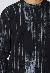 Pull noir en tricot texturé, avec des rayures verticales grises. Coupe classique et encolure ronde. Aucun matériel ou accent visible.