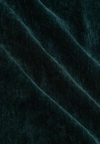 Tiefgrüner Samtstoff mit weicher Textur, der subtile Lichtreflexionen und sanfte Drapierungen aufweist. Ideal für Polsterungen oder Mode.