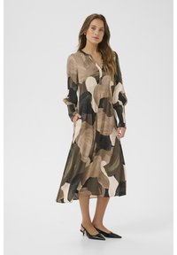 Sraigtinė suknelė su abstrakčiais rudais, smėlio ir juodais raštais. Turi apykaklės iškirptę, ilgomis rankovėmis ir šoninėmis kišenėmis. Dėvima su juodais aukštakulniais.