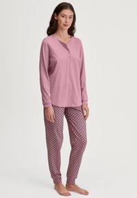 Lichtroze langelijnd shirt met een henley-halslijn. Gedrukt pyjamabroek in roze met een diamanten patroon en donkere accenten.
