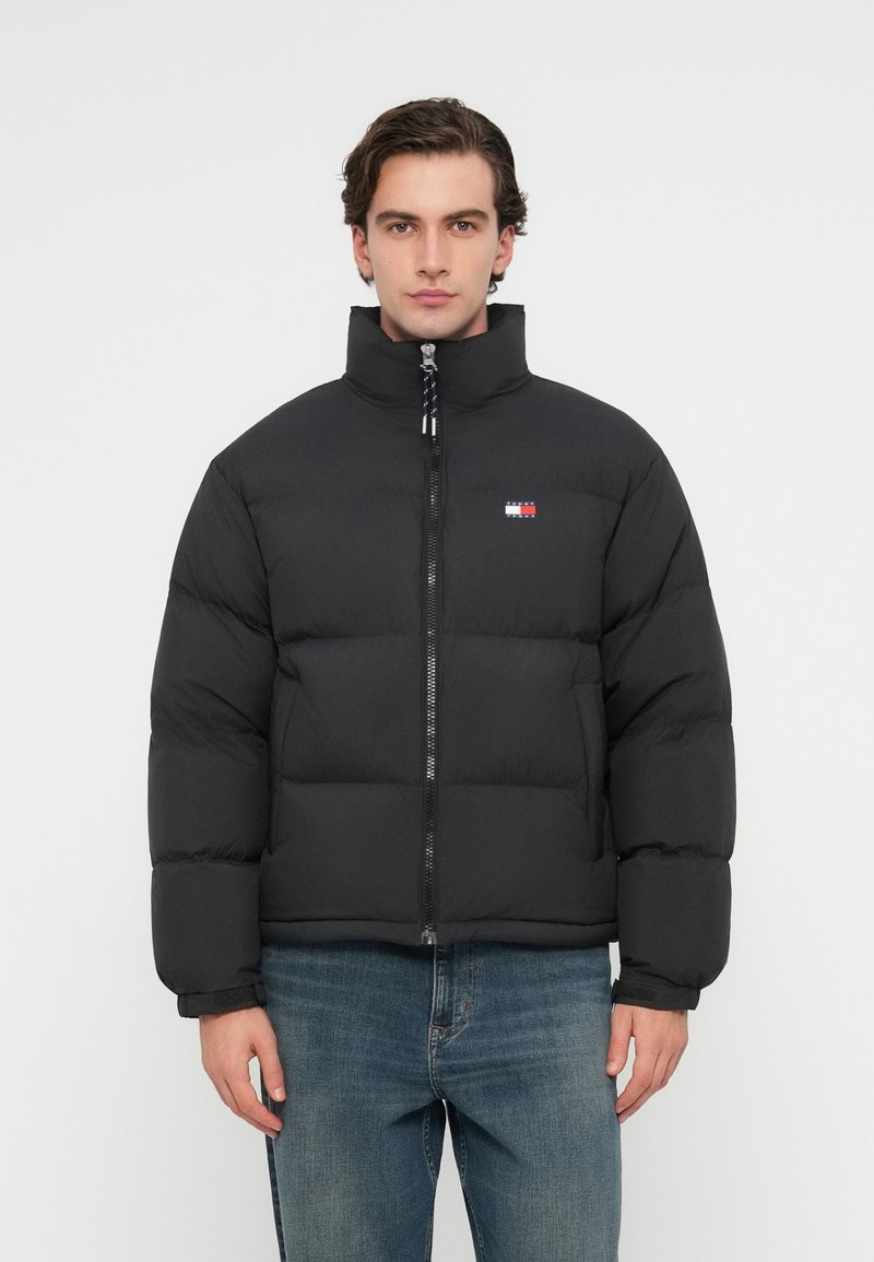 Černá péřovka s vysokým límcem, zapínáním na zip a prošívaným designem. Obsahuje logo nášivku na hrudi a elastické manžety.