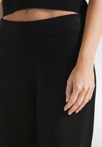 Zwarte wollen broek met een gladde textuur, voorzien van een hoge tailleband en een relaxte pasvorm, gecombineerd met een geribbeld zwart crop top.