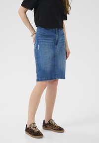 Jeans blyantnederdel i mellemblå med falmede områder og let slid. Kombination med sort top og sneakers med dyreprint.